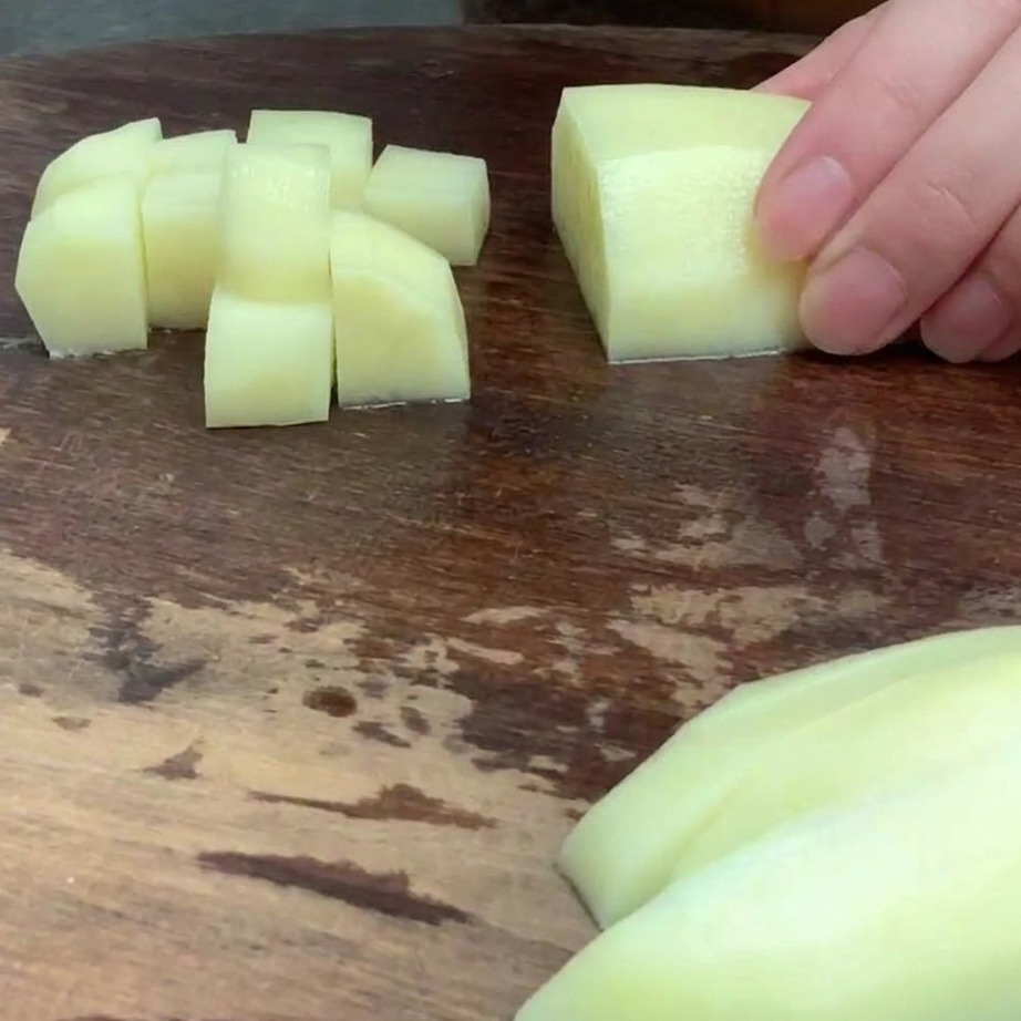 Geschälte Kartoffel in kleinen, gleichmäßigen Würfeln auf einem Holzbrett.