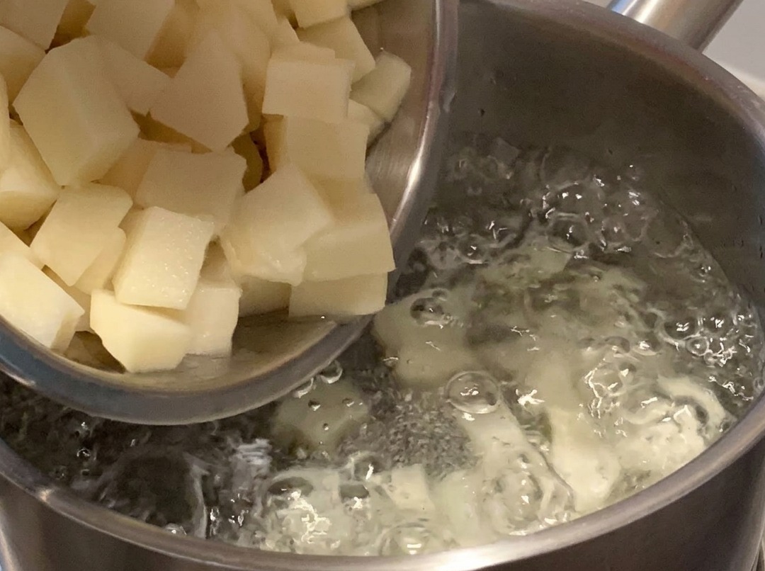 Gewürfelte Kartoffeln kochen in einem Topf mit Wasser auf dem Herd.