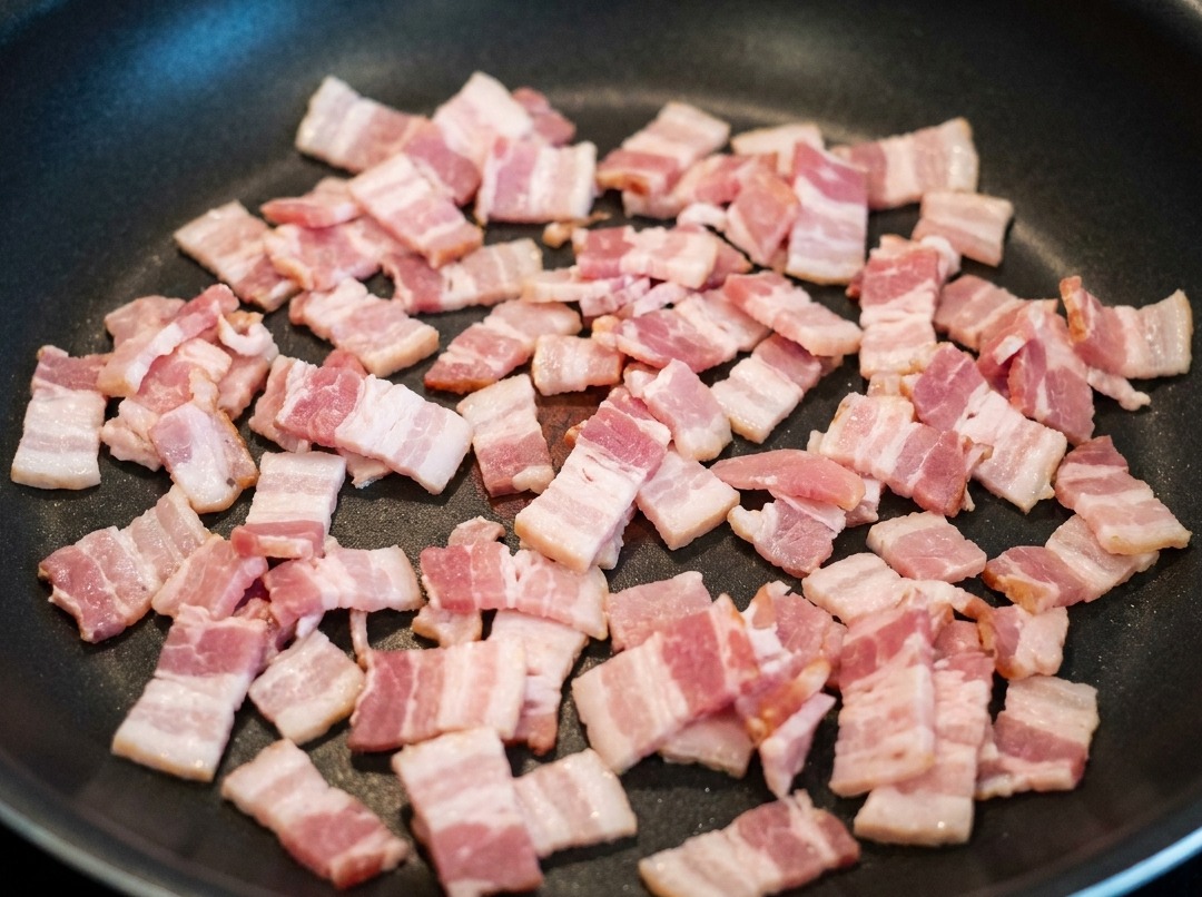 Speckstücke braten in der Pfanne und lassen aromatisches Fett aus.