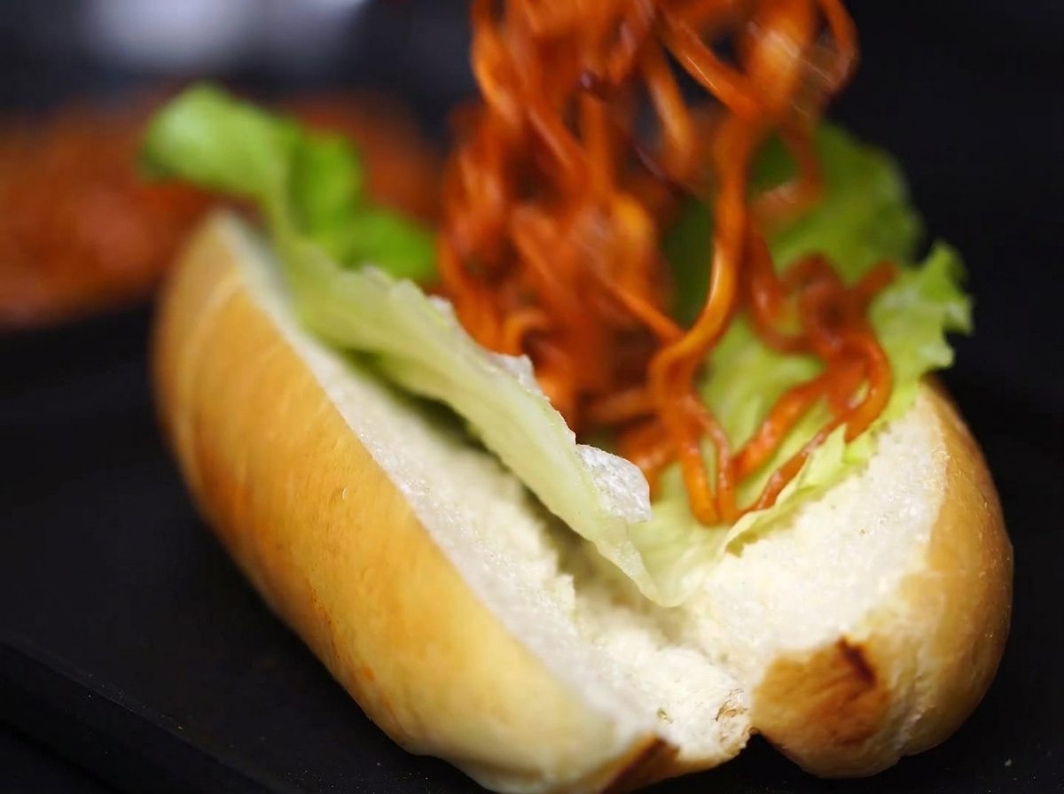 Eine Portion Nudeln mit Soße wird sorgfältig in das mit Salat ausgelegte Brötchen gefüllt.