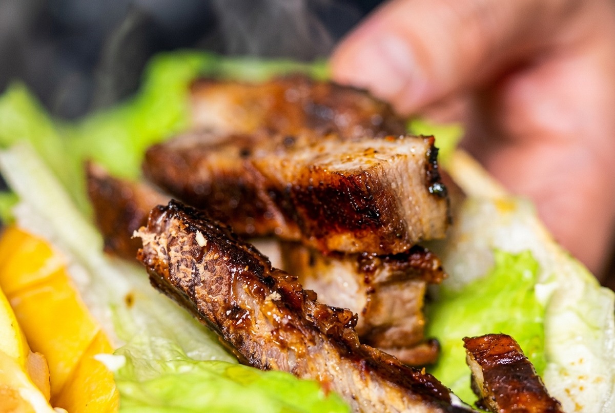 Nahaufnahme eines Hotdog-Brötchens gefüllt mit Nudeln, Garnelen und Steakstreifen.
