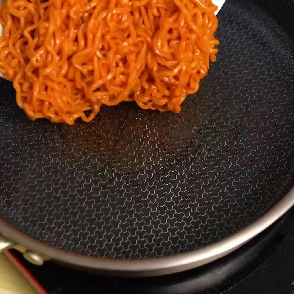 Scharfe Fire-Noodles werden aus einer Schüssel in eine heiße, leere schwarze Pfanne gegeben.