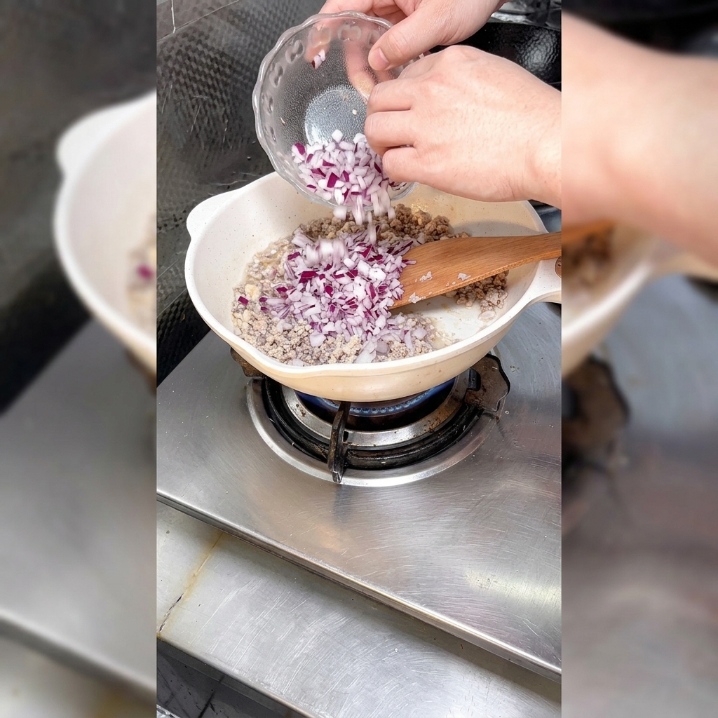 Gewürfelte Zwiebeln werden zu dem angebratenen Hackfleisch in die Pfanne gegeben.