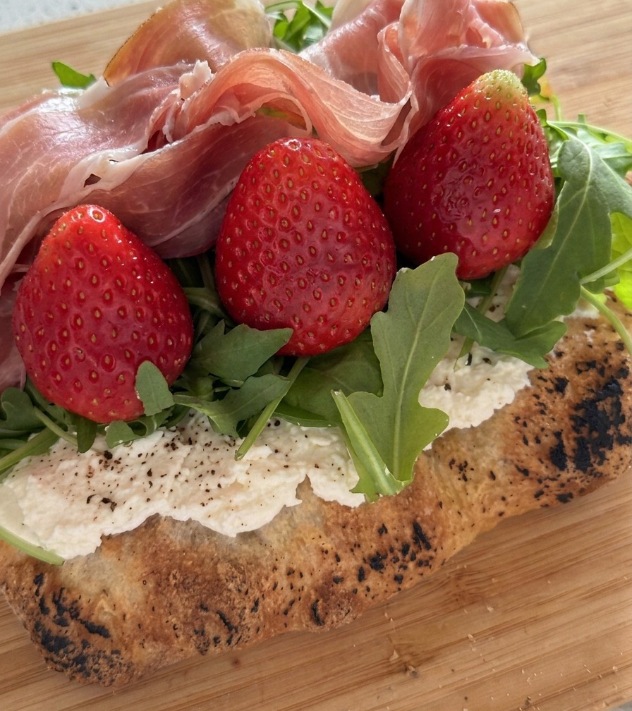 Gefaltete Prosciutto-Scheiben werden auf die Erdbeeren und den Rucola gelegt.