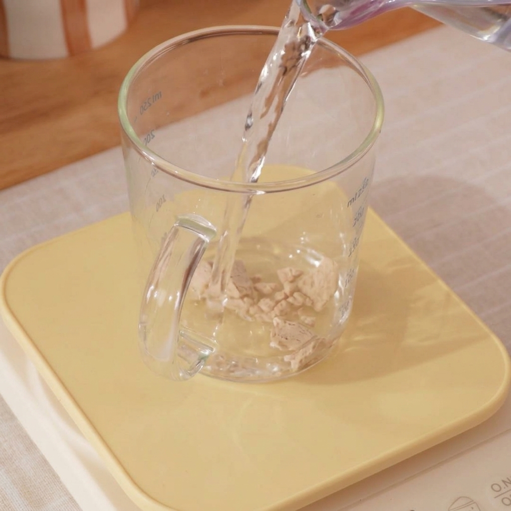 Nahaufnahme eines Messbechers mit Eiswasser und Hefe, die mit einem Schneebesen verrührt wird.