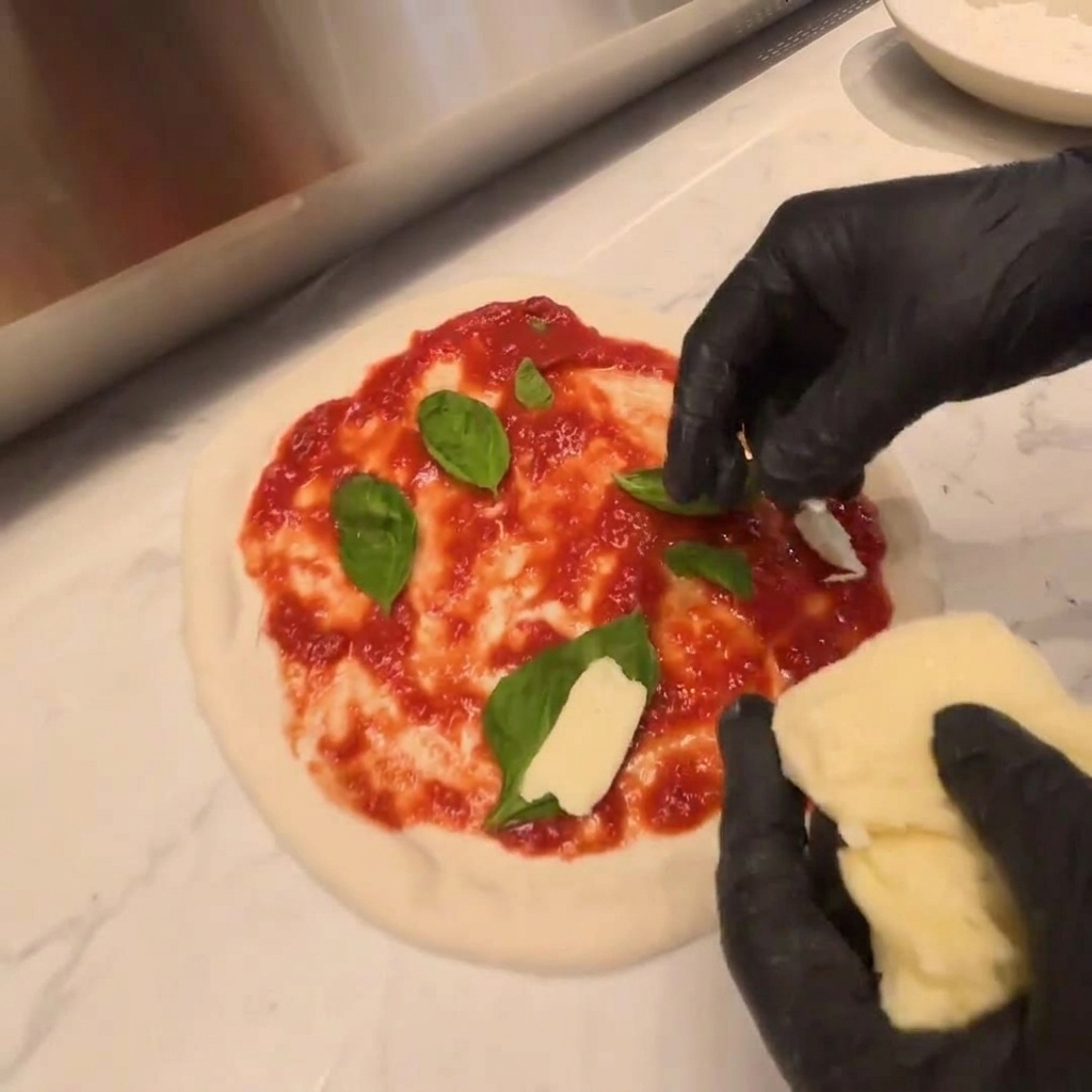 Stücke von frischem Mozzarella werden über die Rucola auf dem rohen Teig gelegt.