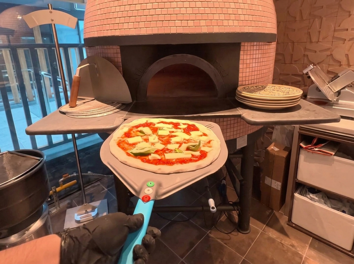 Eine Pizza auf einem Metallschieber wird in einen Holzofen geschoben.