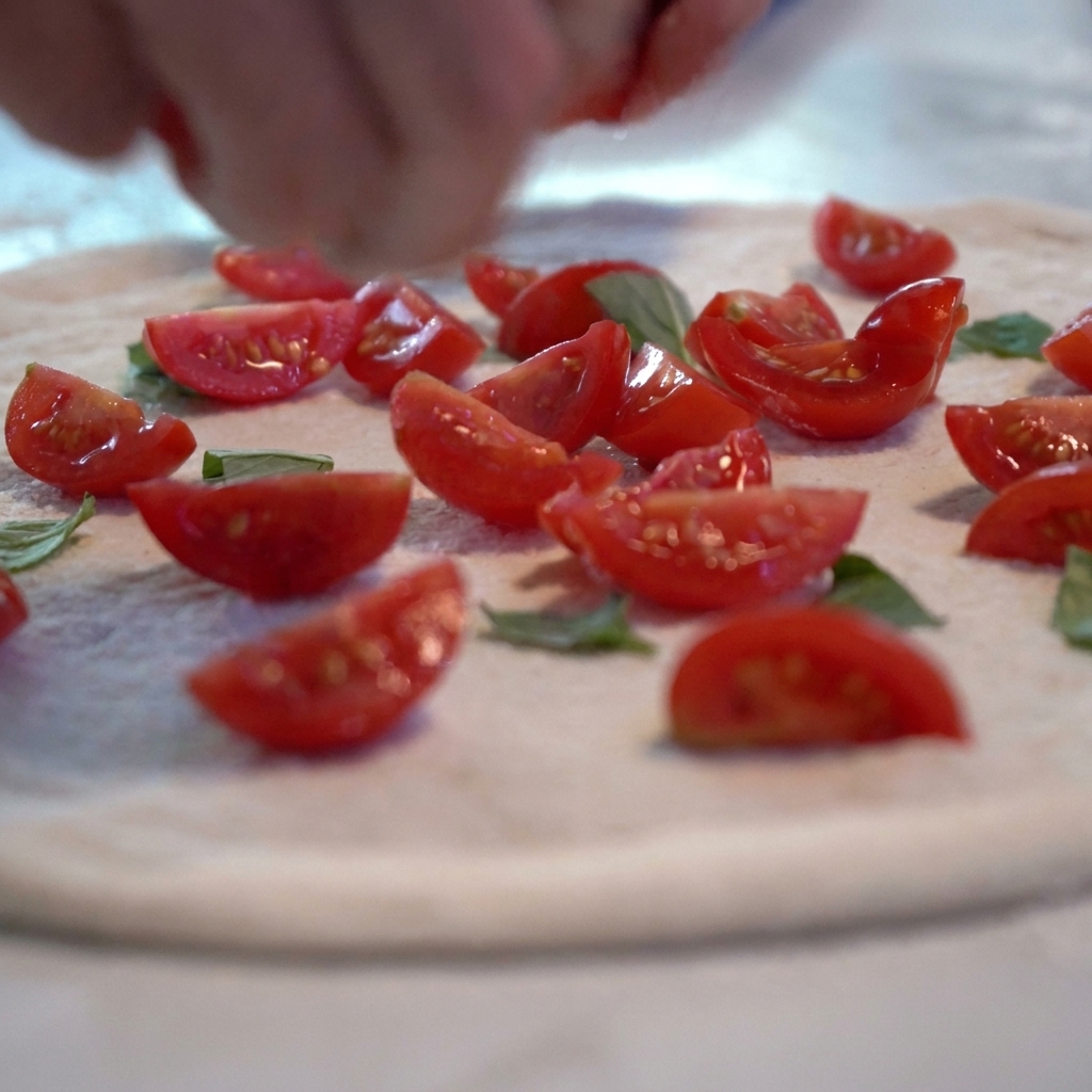 Tomatensoße und frische Tomatenscheiben werden auf dem rohen Pizzaboden verteilt.