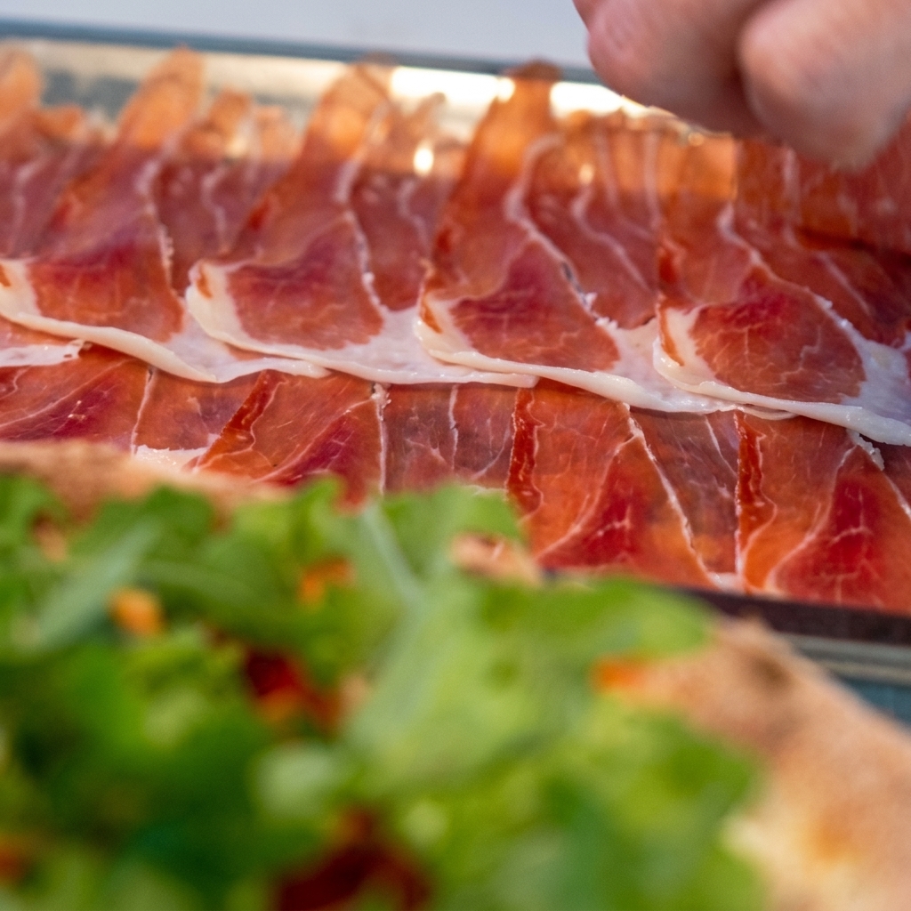 Dünne Scheiben Prosciutto werden vorsichtig auf der Rucola-Pizza drapiert.