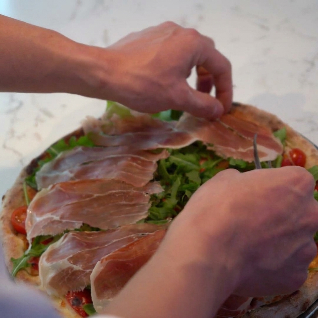 Geriebener Parmesan wird über die Pizza gestreut und bedeckt den Prosciutto und Rucola.