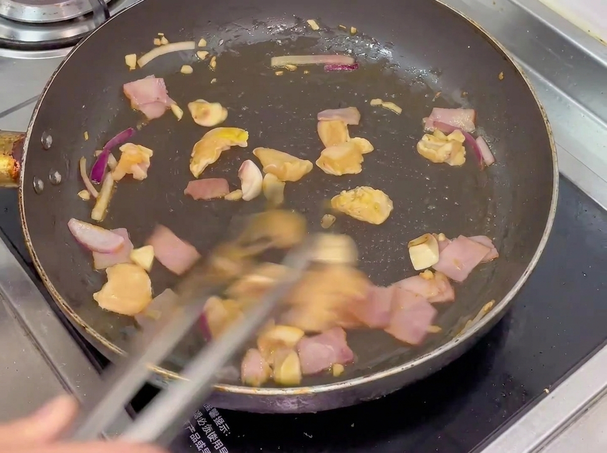 Eine Mischung aus Hähnchen, Speck, Pilzen und Zwiebeln wird in einer heißen Pfanne geschwenkt.
