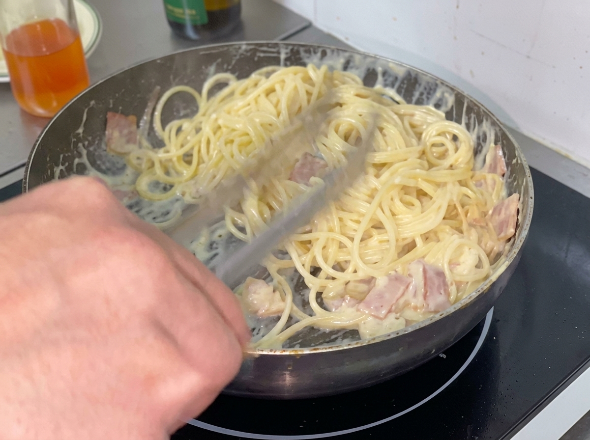 Eine Portion gekochter Spaghetti wird in eine cremige Sauce in einer Bratpfanne gegeben.