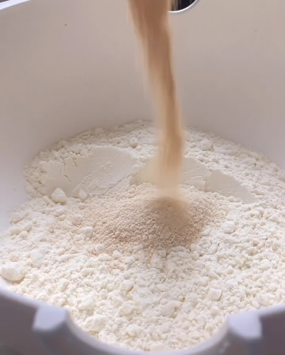 Trockenhefe wird in eine große weiße Schüssel mit Mehl gegossen.