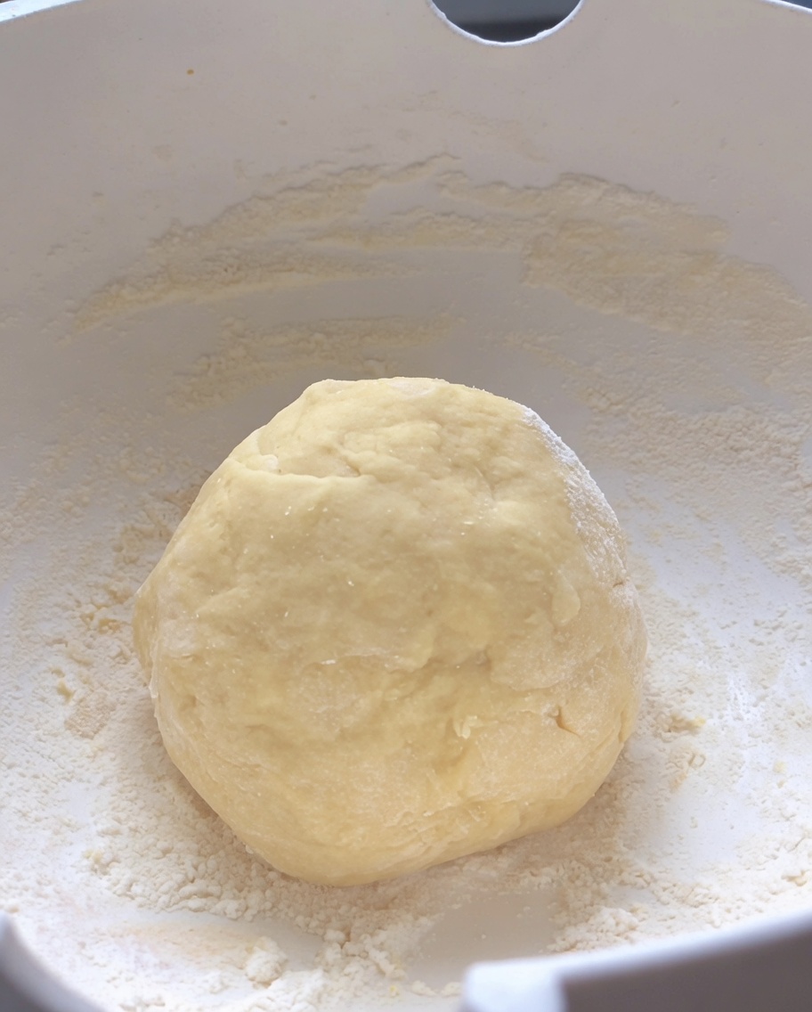 Eine glatte, runde Kugel aus geknetetem rohem Teig ruht in der Mitte einer weißen Rührschüssel.