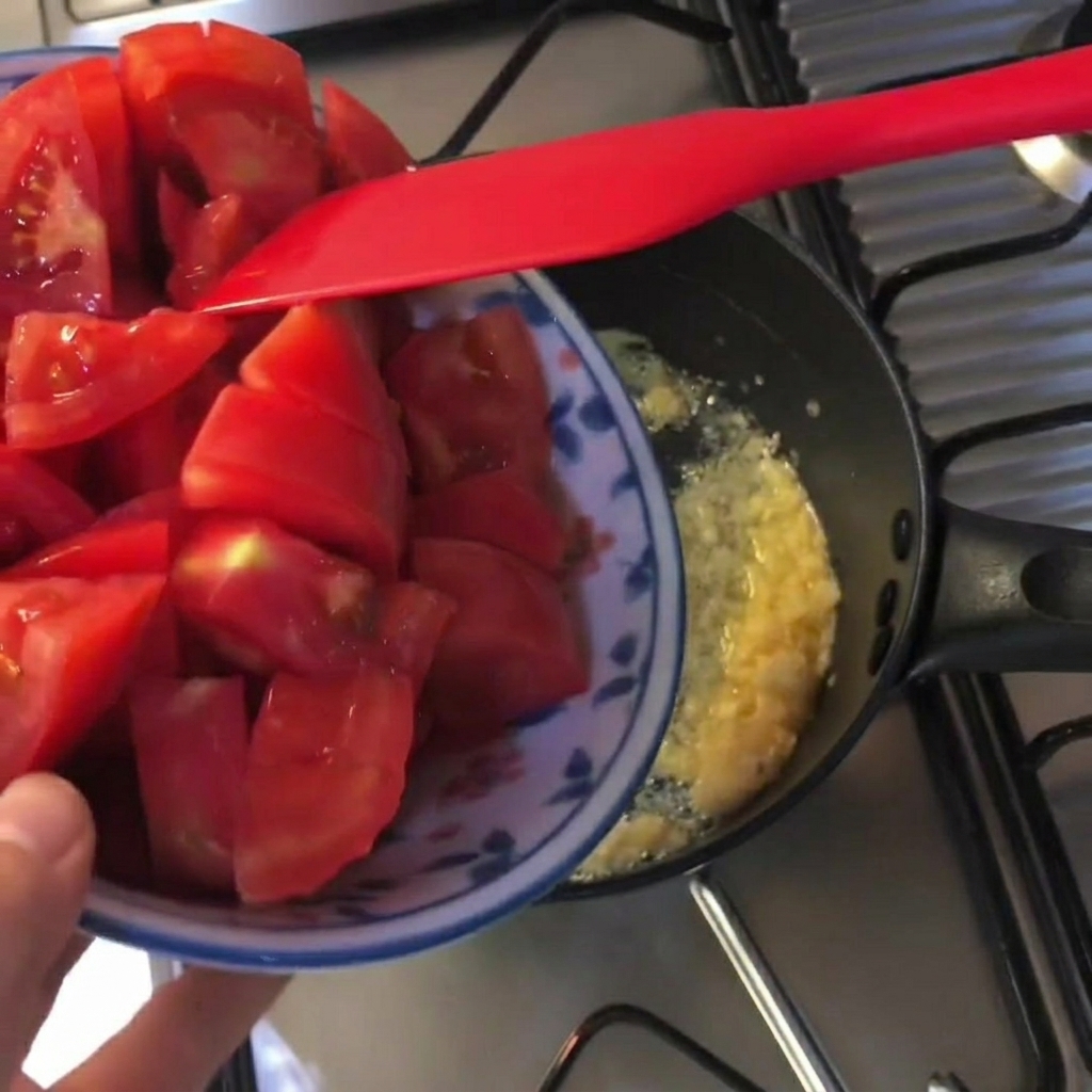 Frische rote Tomatenwürfel werden in einen schwarzen Topf mit geschmolzener Butter und gehacktem Knoblauch gegeben.