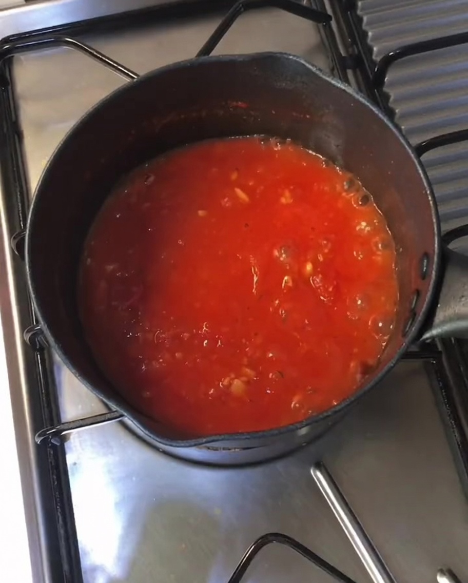 Dicke, blubbernde rote Tomatensoße köchelt in einem schwarzen Topf auf dem Herd.