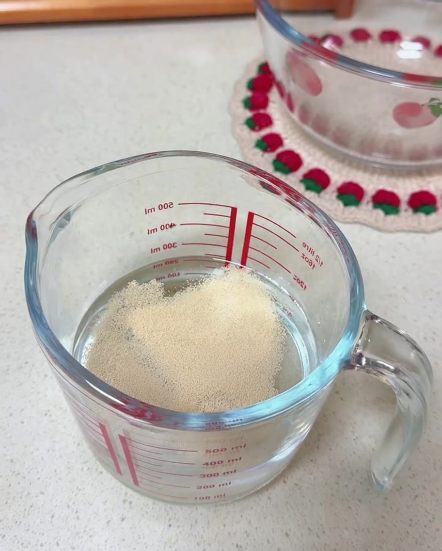 Trockenhefekörner auf der Wasseroberfläche in einem durchsichtigen Glasmessbecher.