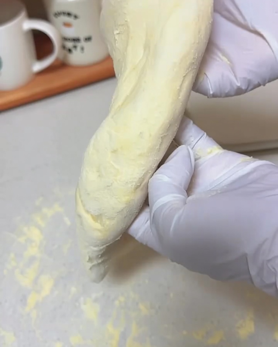 Hände halten ein weiches Teigstück senkrecht und lassen es zu einem dünnen Pizzaboden ausziehen.