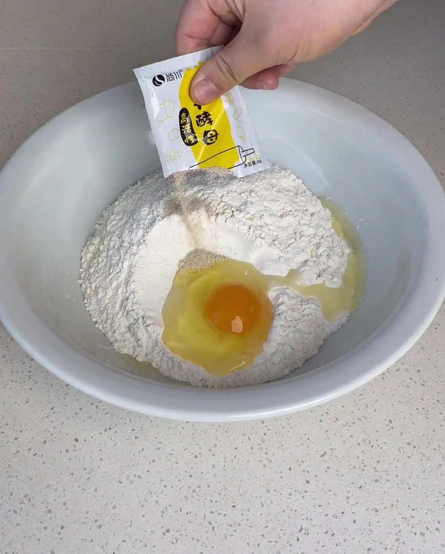 Trockenhefe, weißer Zucker und Salz werden über das Mehl mit dem aufgeschlagenen Ei in der Mitte gestreut.