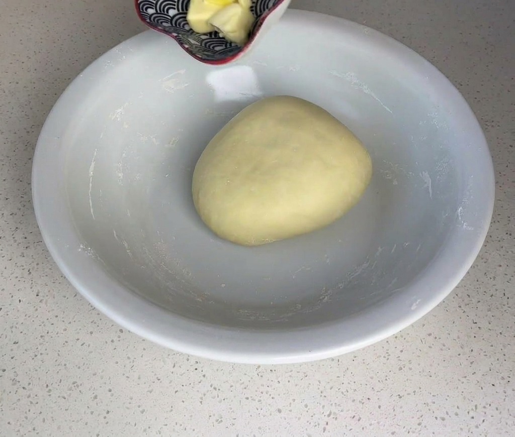 Kleine Würfel gelber Butter werden aus einer kleinen Schüssel auf eine glatte Teigkugel gegeben.