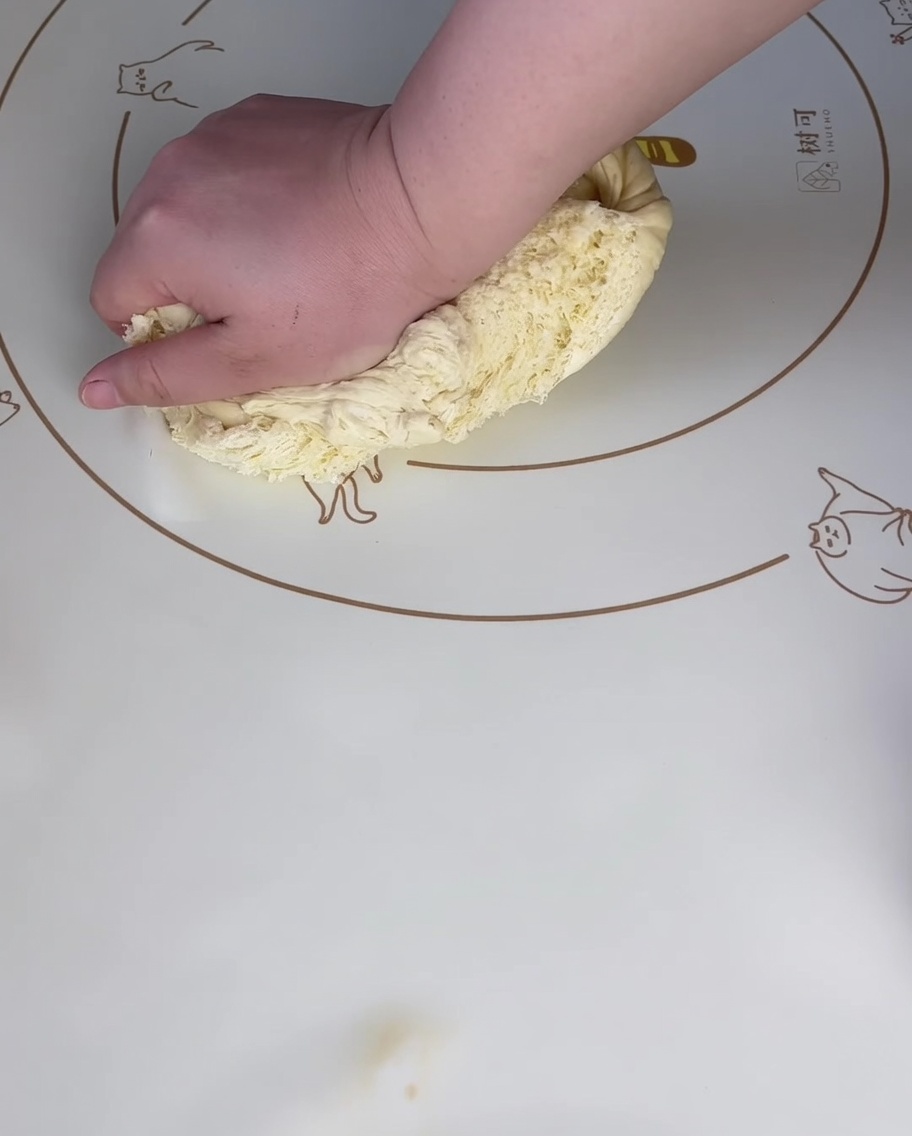 Eine Hand drückt fest auf ein Stück aufgegangenen Teig auf einer gemusterten Silikonmatte, um die Luft herauszudrücken.
