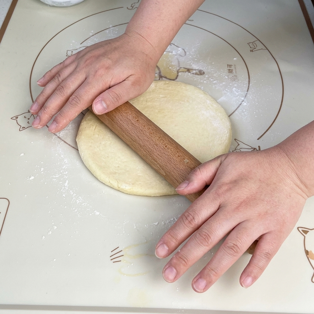 Ein hölzernes Nudelholz rollt ein weiches Stück Pizzateig auf einer Antihaft-Backmatte zu einer gleichmäßigen quadratischen Form aus.