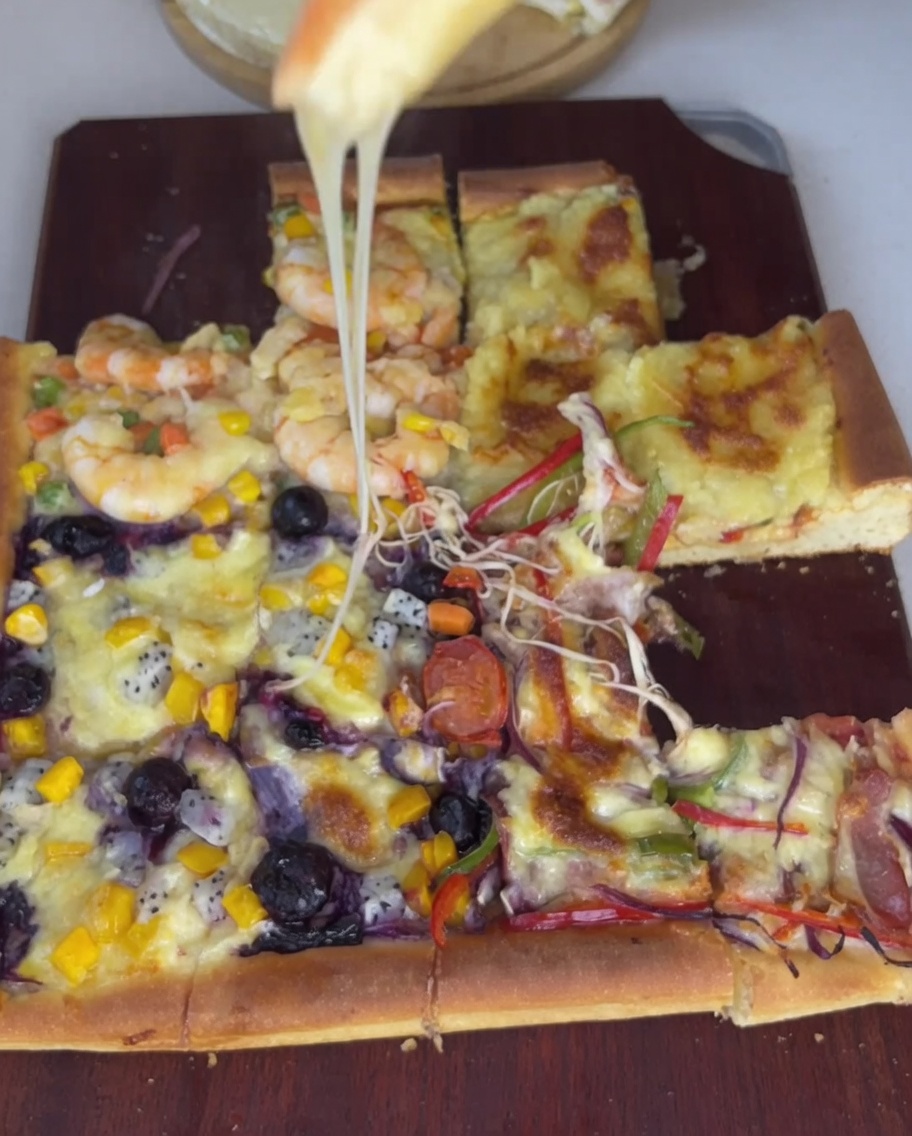 Nahaufnahme von Speckstreifen, roten Zwiebeln und bunten Paprika, die sorgfältig auf dem Pizzateigviertel angerichtet werden.