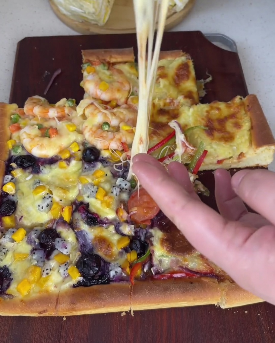 Cremiges Durian-Fruchtfleisch wird mit einem Löffel gleichmäßig auf dem vierten Abschnitt des Pizzateigs verteilt.