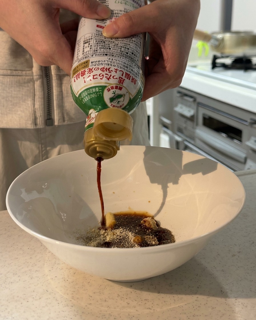Hände gießen Sojasauce aus einer Flasche in eine Schüssel mit trockenen Gewürzen und Paste.
