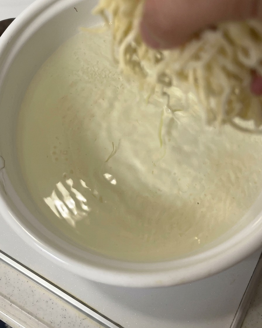 Eine Hand gibt eine Portion frische Ramen-Nudeln in einen Topf mit sprudelnd kochendem Wasser.