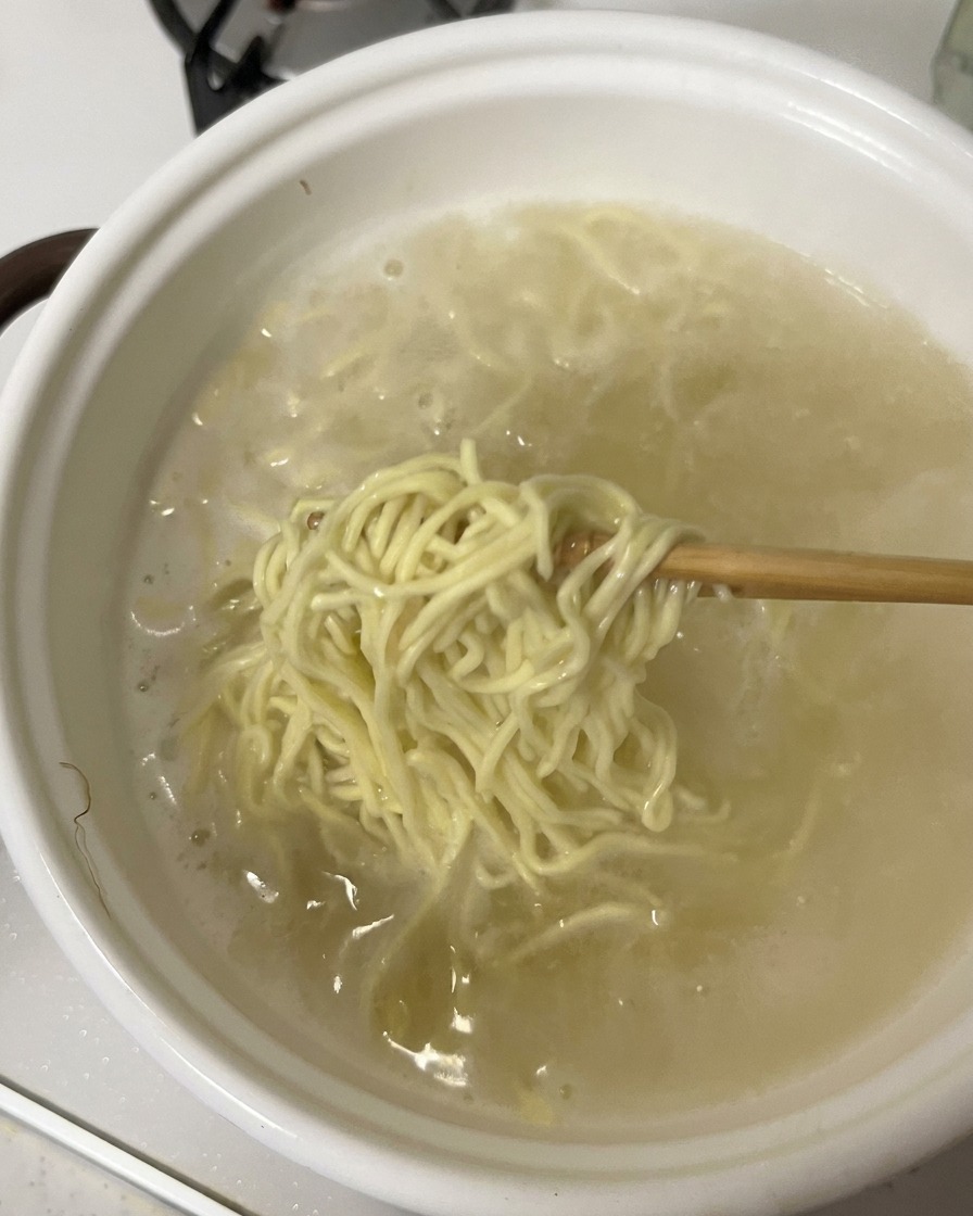 Stäbchen heben eine Portion gekochte Nudeln aus einem weißen Topf.