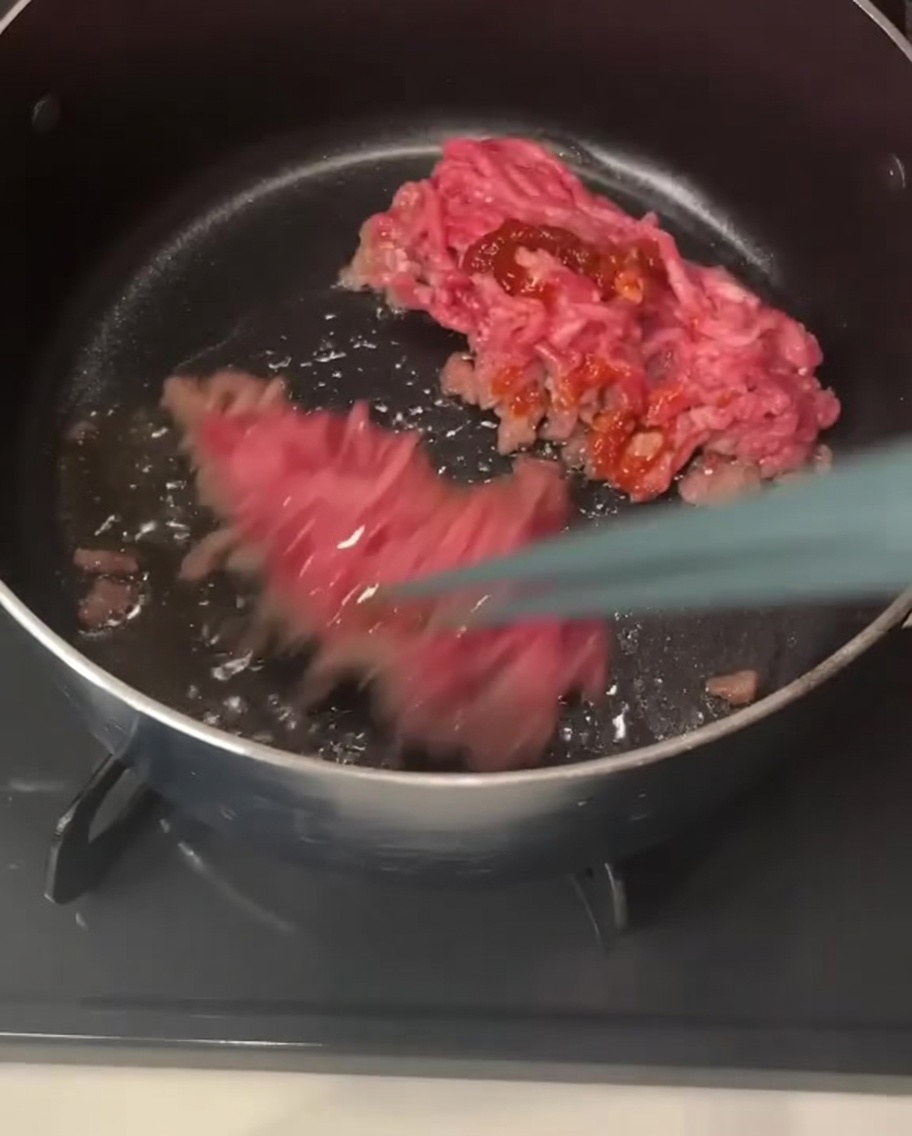 Stäbchen heben und rühren Stücke von Schweinehackfleisch um, die in einem Topf mit rötlicher Chilipaste überzogen sind.