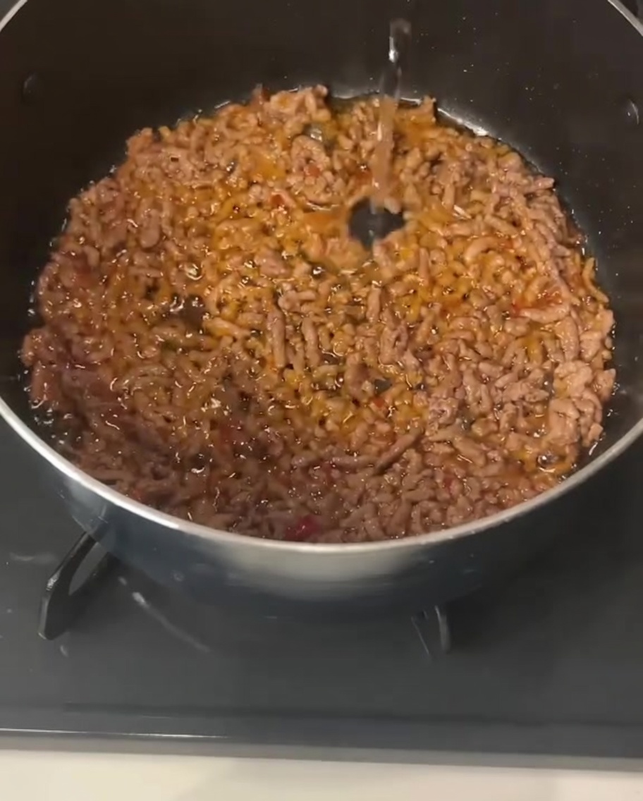 Klare Flüssigkeit wird in einen Topf mit dem gebratenen, gewürzten Schweinehackfleisch gegossen.
