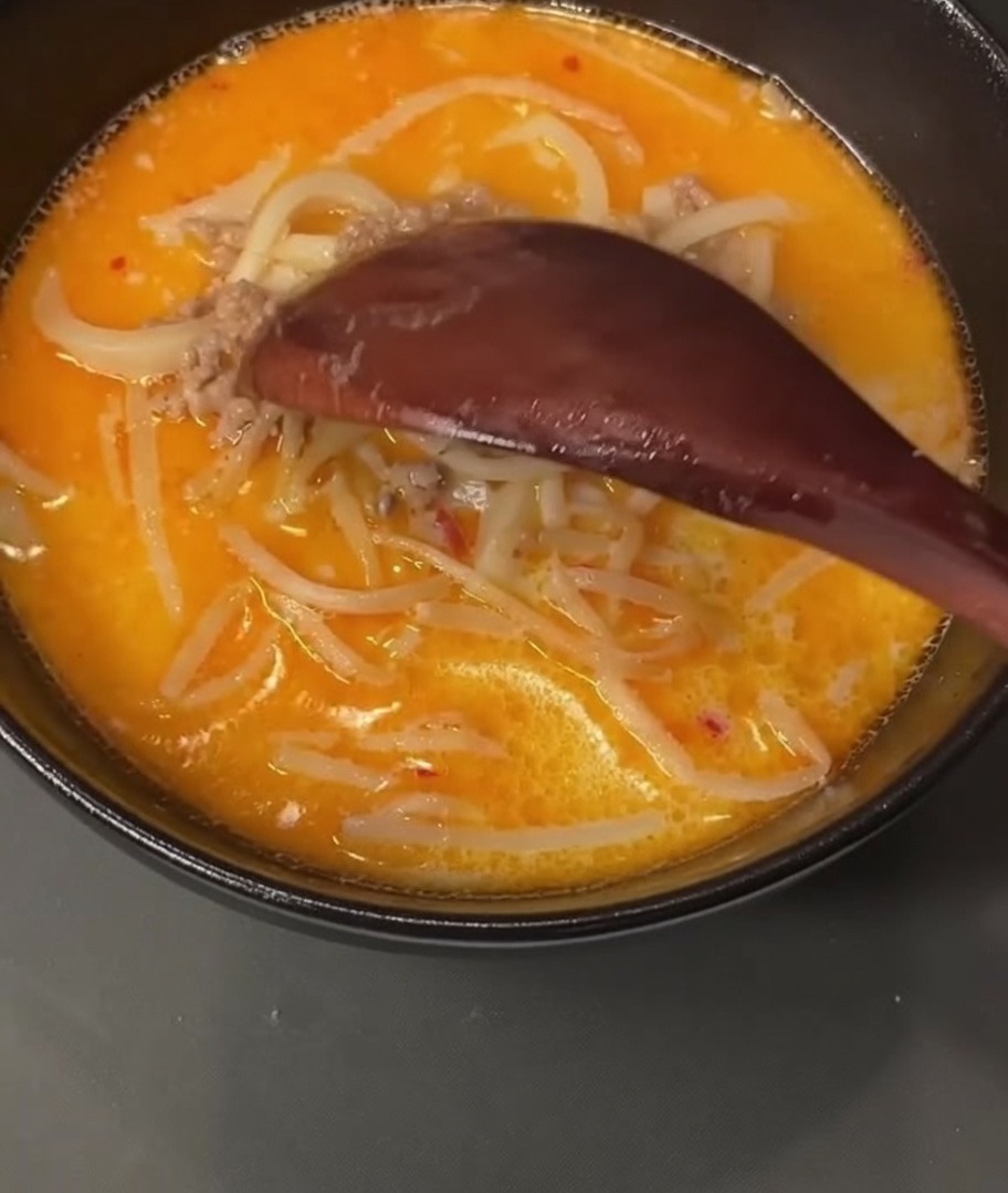 Ein Holzlöffel schöpft gekochtes Schweinehackfleisch aus einem mit Brühe gefüllten Topf.
