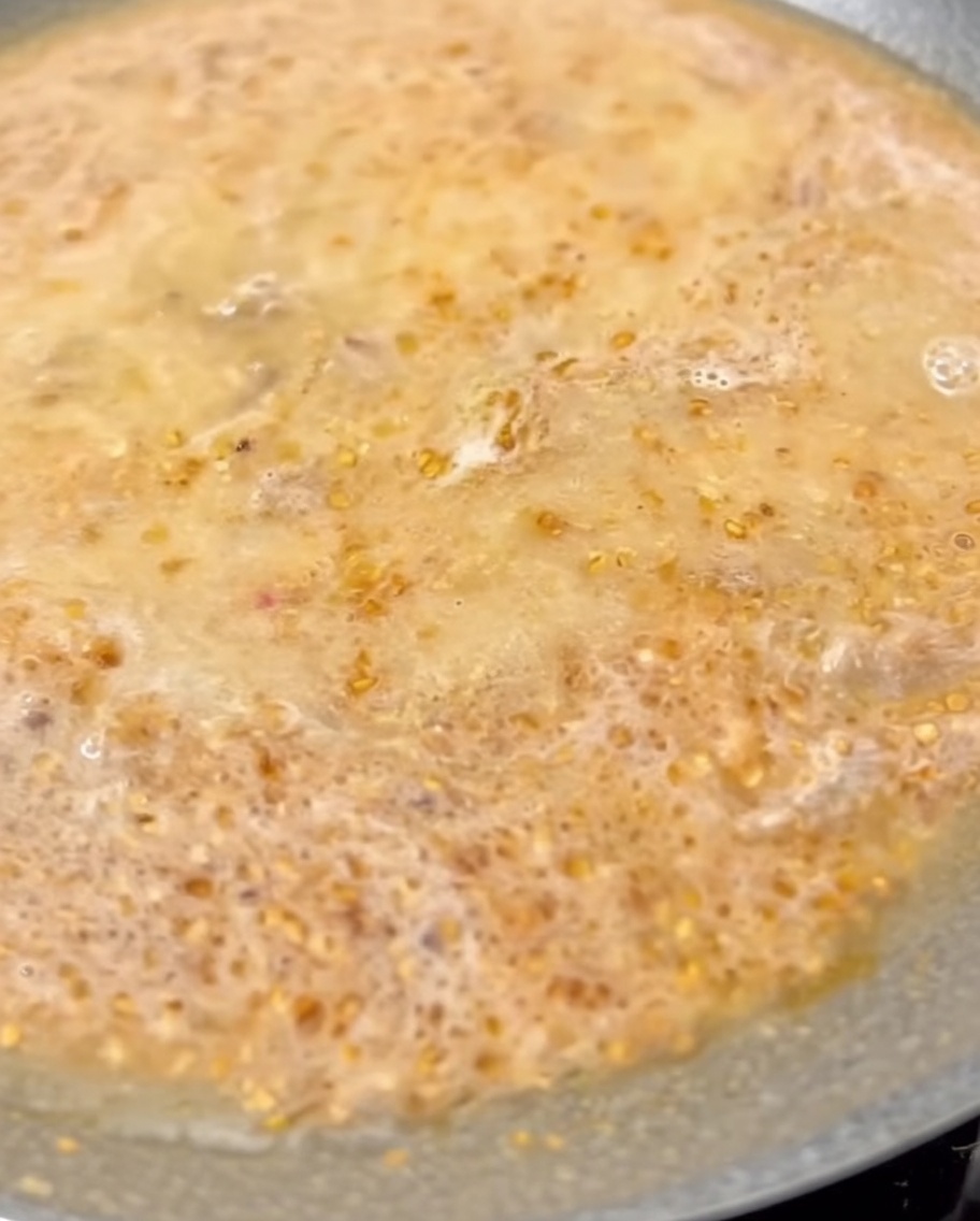 Milch wird in die köchelnde Tantanmen-Brühe in der Pfanne eingerührt.