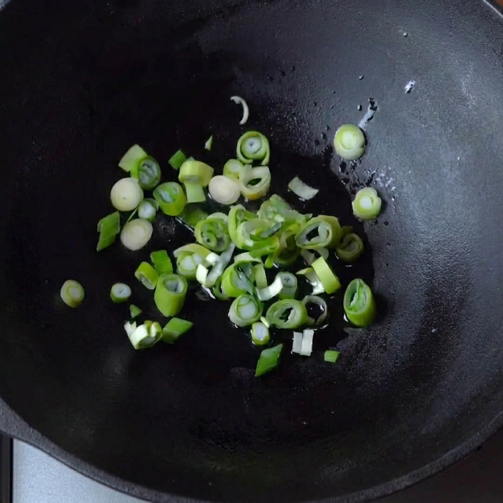 Frühlingszwiebeln brutzeln in einer kleinen Menge Öl in einem gusseisernen Wok.