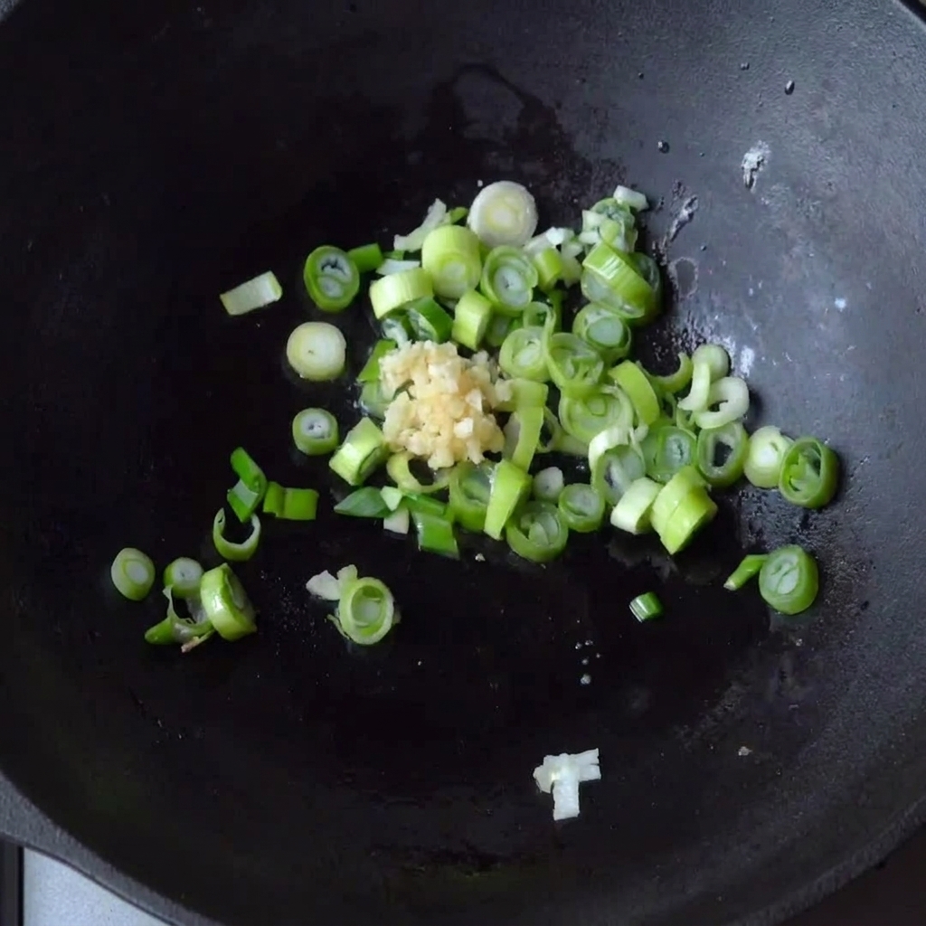 Gehackter Knoblauch wird zu den bereits schmorenden Frühlingszwiebeln in die Pfanne gegeben.
