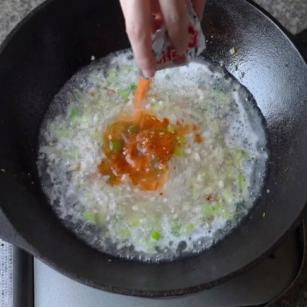 Ramen-Gewürzpulver wird in die siedende Brühe im Wok gestreut.