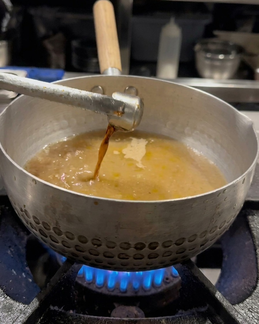 Sojasauce wird in die Brühe geträufelt und mit einem Schneebesen vermengt.