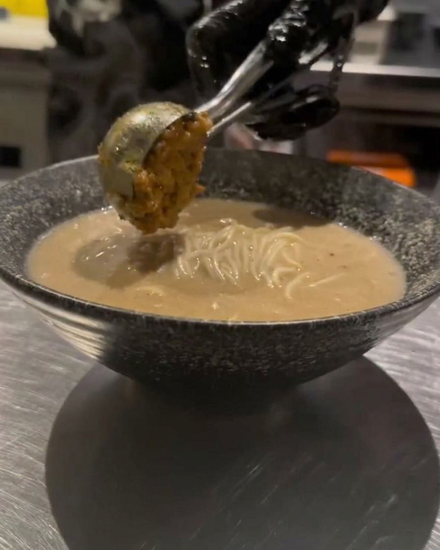 Ein Löffel gewürztes Hackfleisch wird vorsichtig auf die Ramen gegeben.