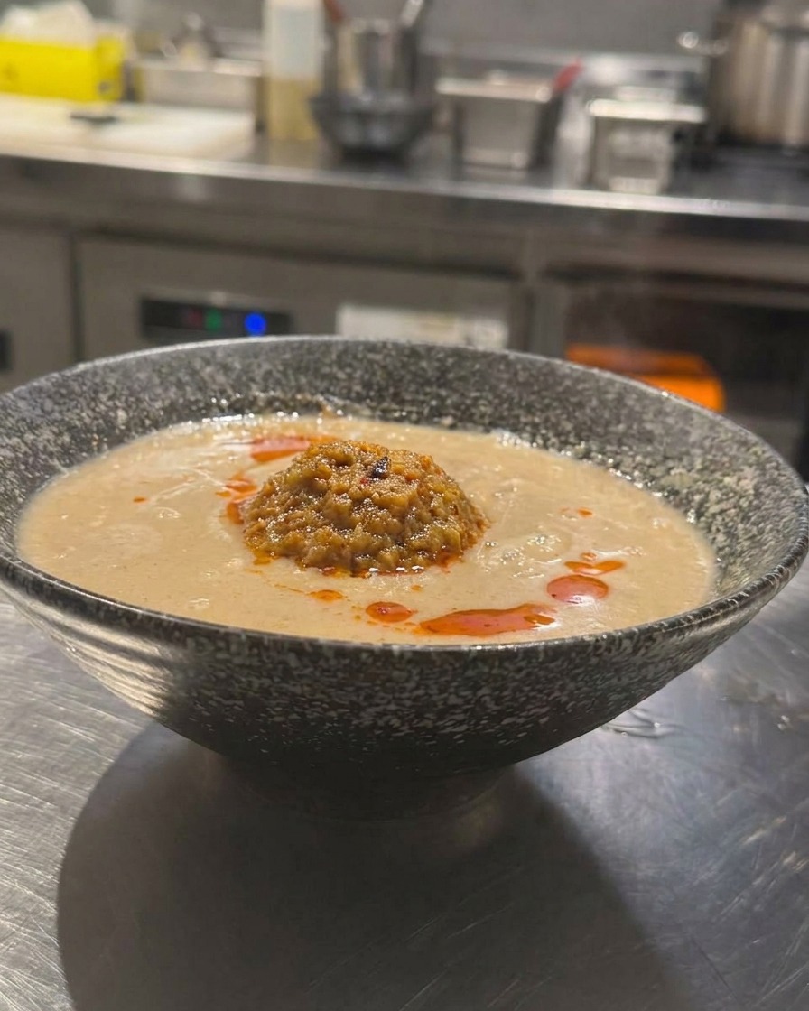 Eine Schüssel japanisches Tan Tan Ramen mit cremiger Brühe, Hackfleisch und einem Schuss leuchtend rotem Chiliöl.