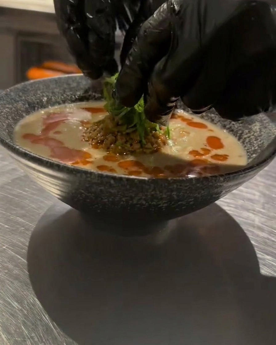 Hände platzieren fein geschnittene Frühlingszwiebeln als letztes Garnitur-Element auf dem Ramen.