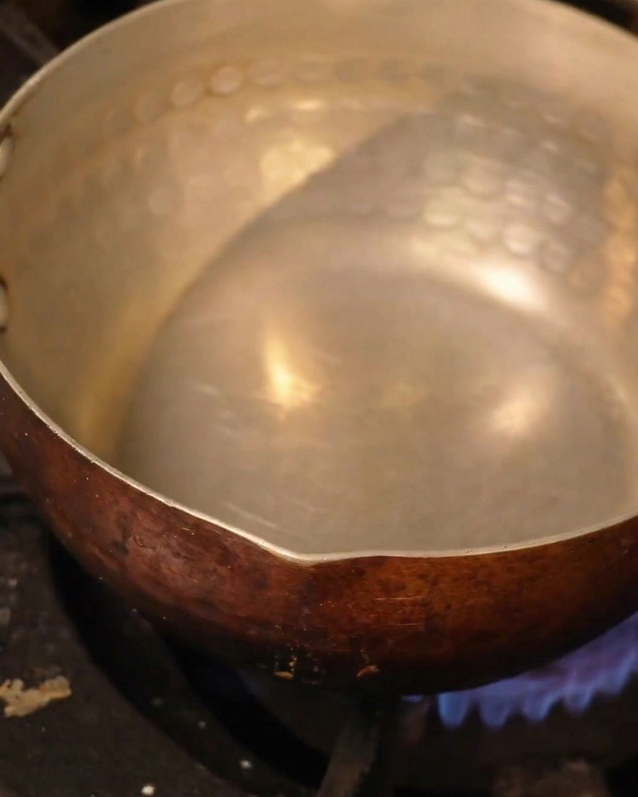 Ein hämmerter Metalltopf mit Flüssigkeit auf einer Herdplatte.