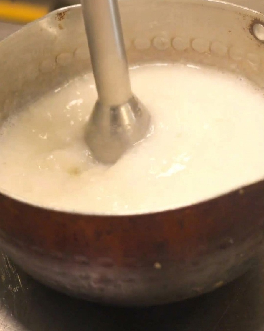 Ein Stabmixer beim Aufschäumen von cremiger Hähnchenbrühe.