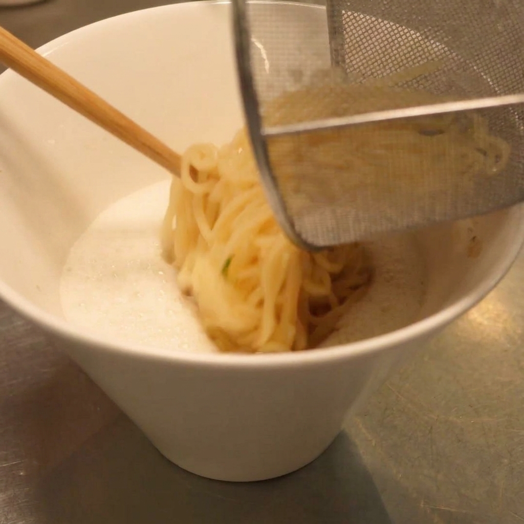 Abtropfende Nudeln werden mit einem Sieb in die Schüssel mit cremiger Suppe gegeben.
