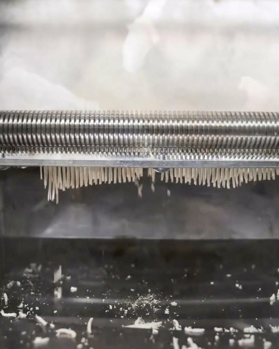 Eine Nudelmaschine walzt und schneidet den Teig in dünne Ramen-Fäden.