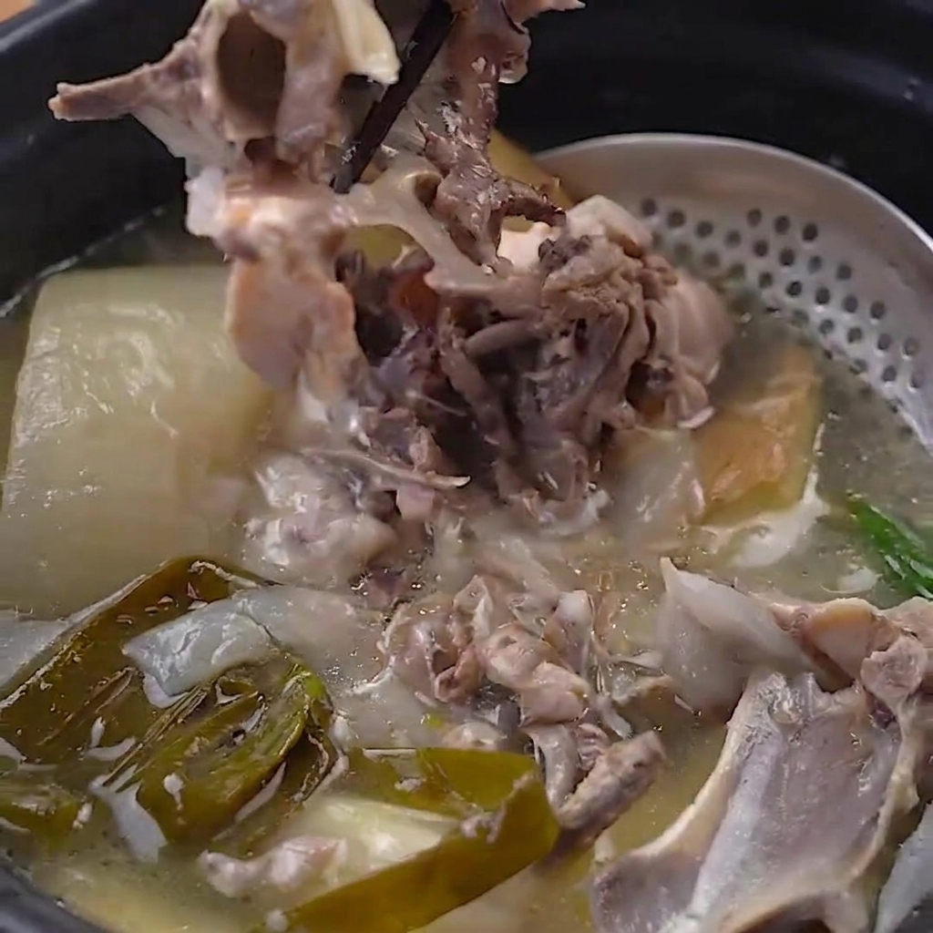 Zartes Hühnerfleisch wird mit schwarzen Stäbchen von den gekochten Knochen gelöst.