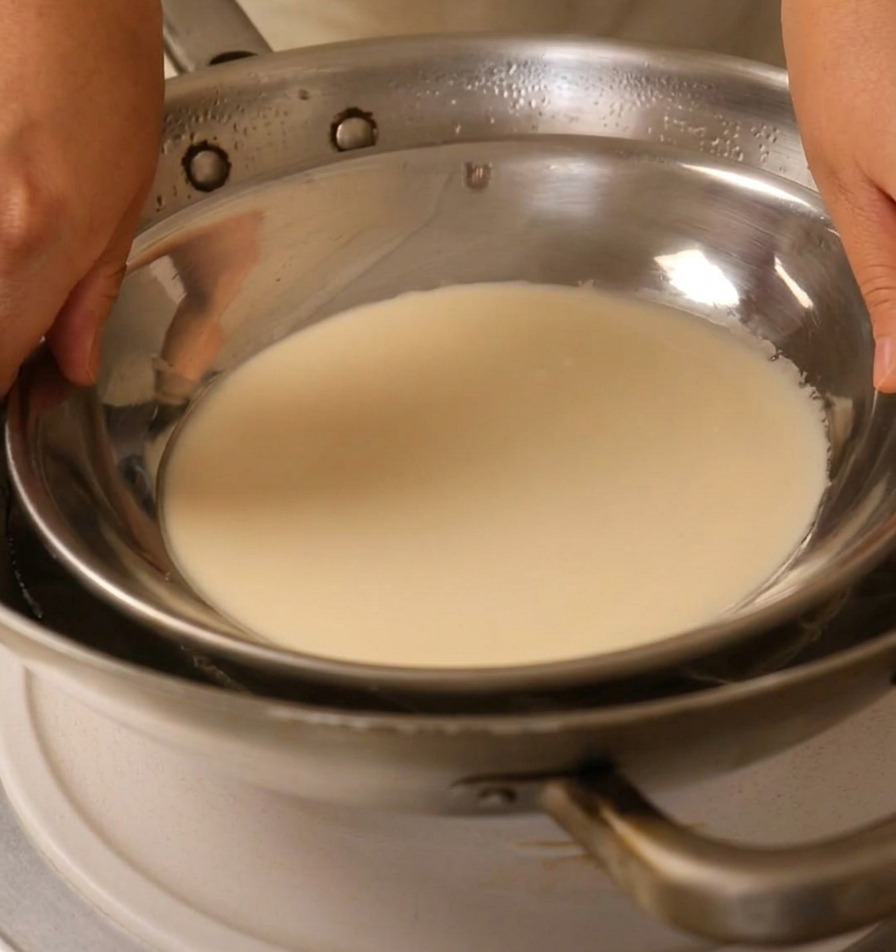 Hände platzieren eine Metallplatte mit Teig über einem Wok mit kochendem Wasser.