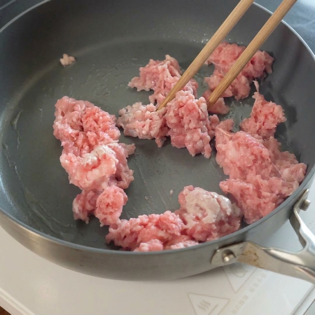 In Scheiben geschnittener Knoblauch wird zum gebratenen Hackfleisch in die Pfanne gegeben.