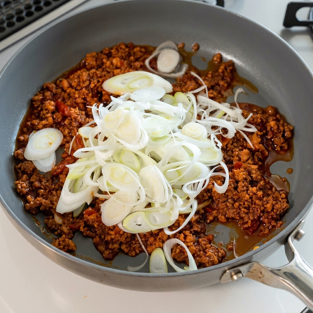Eine große Menge geschnittene Frühlingszwiebeln wird zur Fleischsauce gegeben.